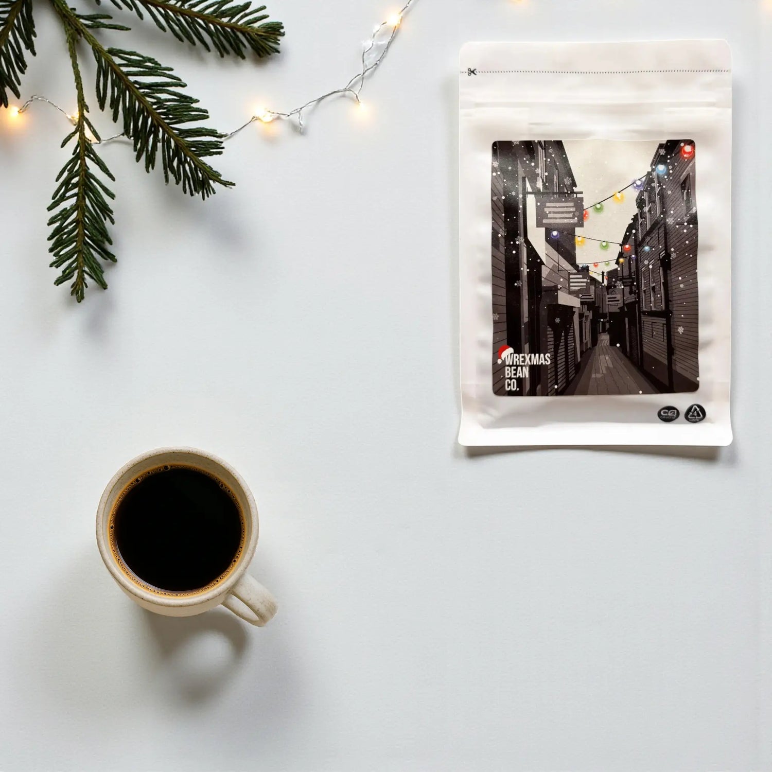 The Wrexham Bean Christmas Blend coffee bag on a bright surface, styled with gentle fairy lights and a spruce branch.