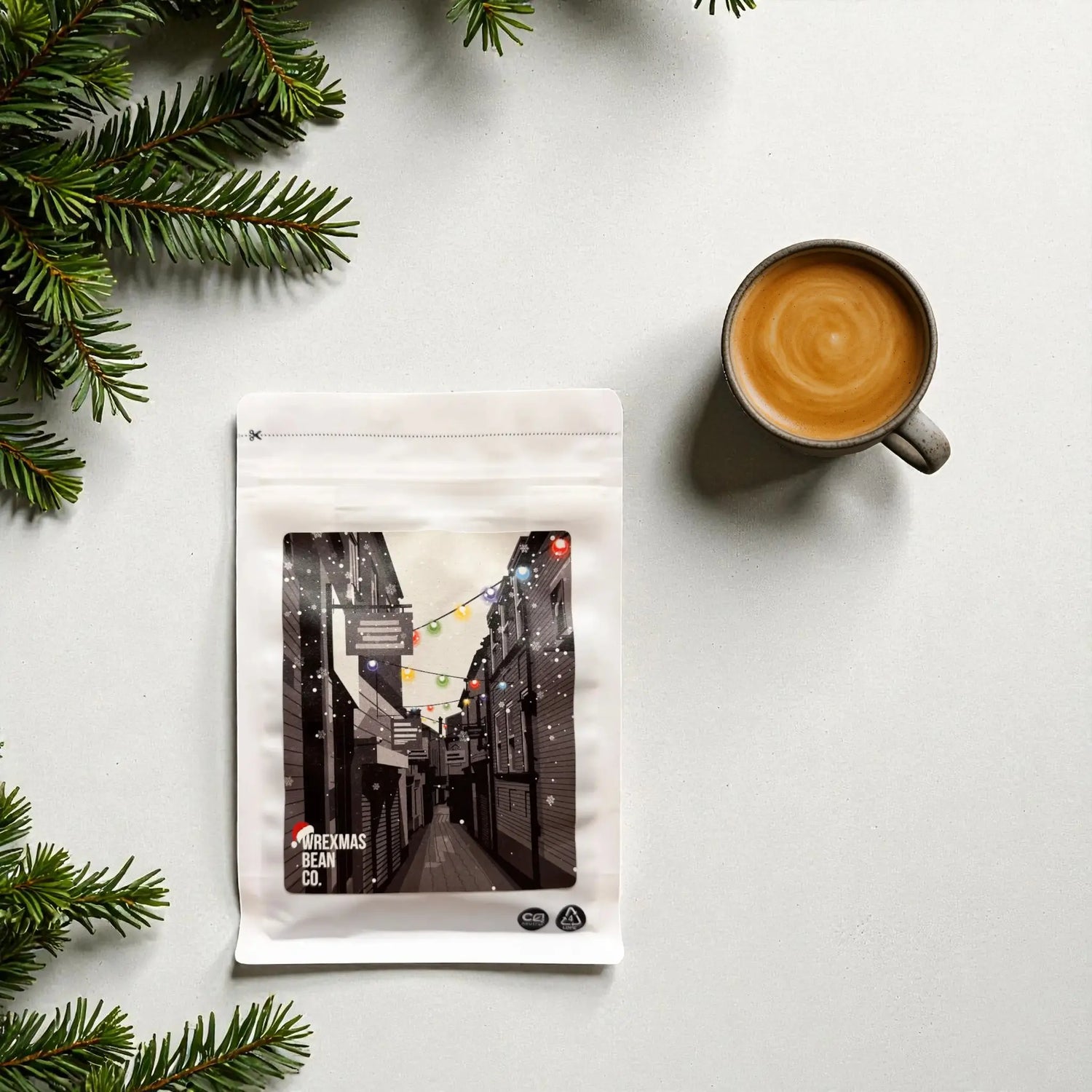 A minimalist winter scene showing the Wrexham Bean Christmas Blend coffee bag with a cup of black coffee on a clean background.